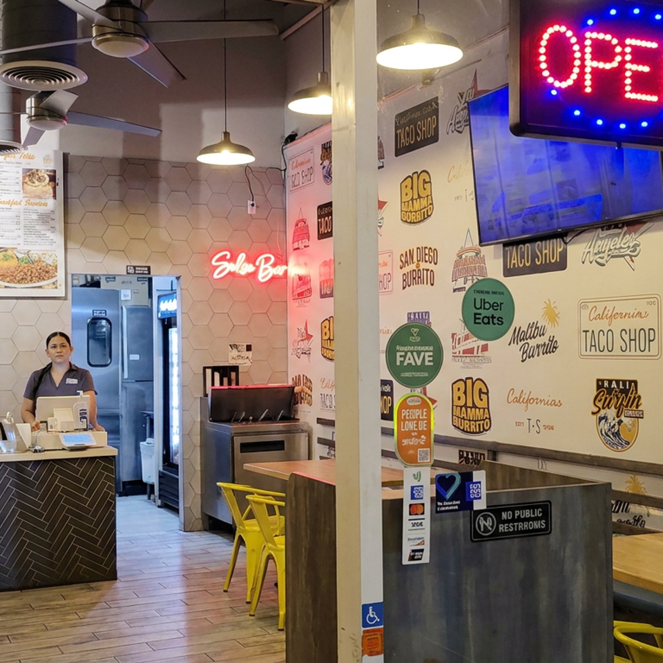 Bright taco shop interior with open sign, colorful burrito-themed walls, menu boards, counter, and employee.